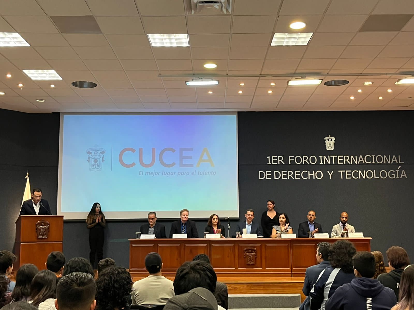 Mesa principal del I Foro con letrero 1ER FORO INTERNACIONAL DE DERECHO Y TECNOLOGÍA y pantalla CUCEA